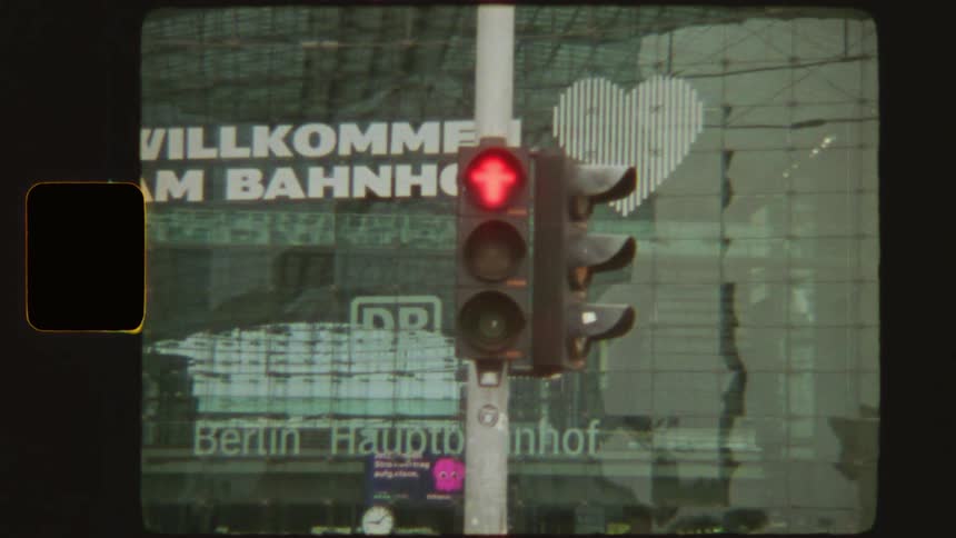 Vintage super 8mm film footage of an Ampelmännchen traffic light changing from red to green in front of the Berlin Hauptbahnhof train station