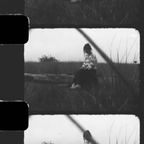 Vintage black and white filmstrip footage shows a young woman in a striped sweater smiling peacefully while sitting in a grassy field
