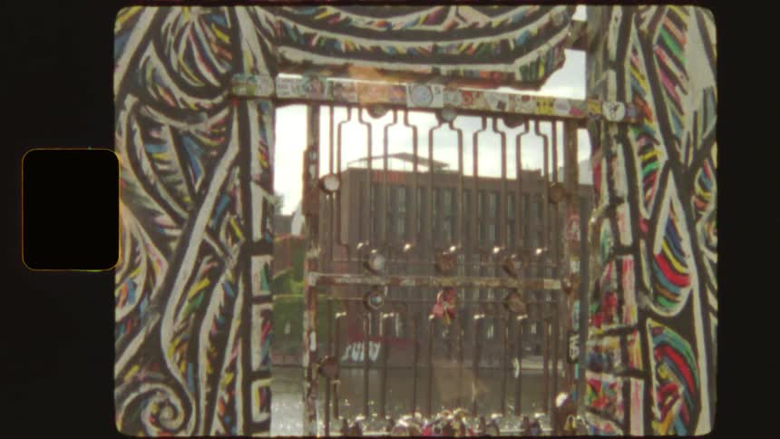 Vintage film shot tilts up on a graffiti-covered gate at the East Side Gallery in Berlin, ending with a bright film burn