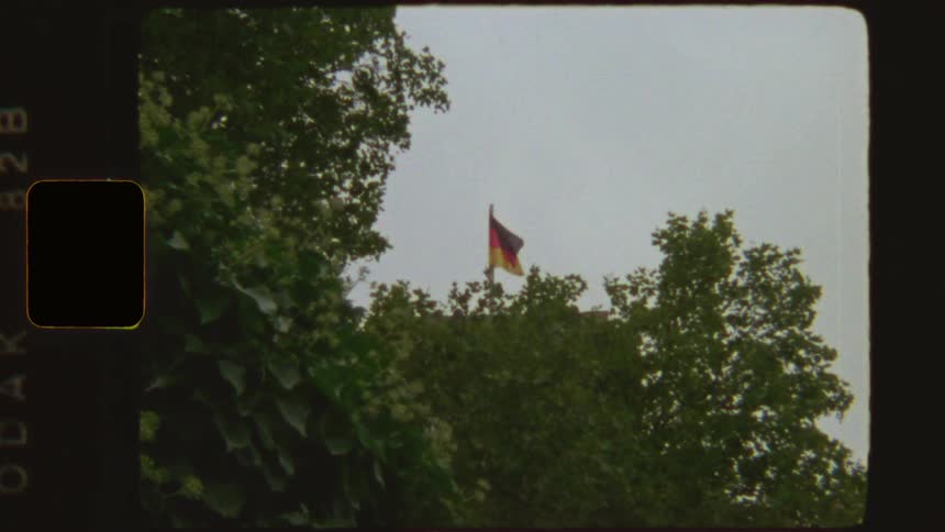Vintage 8mm footage shows the German flag waving in the wind above green trees against an overcast sky