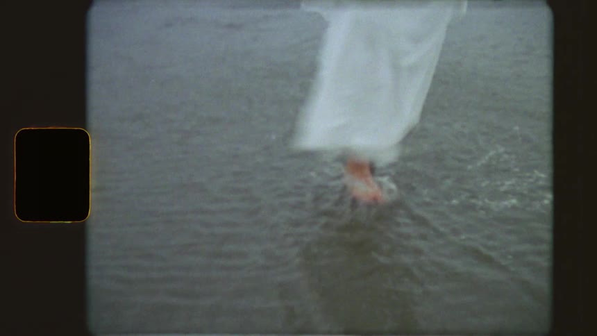 Vintage 8mm film shows a woman's bare feet splashing as she walks in the shallow waves of the ocean