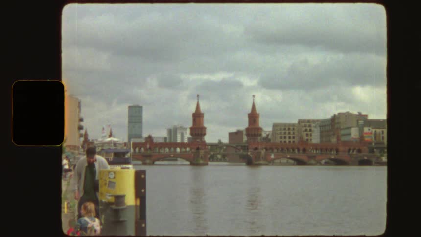 A vintage Super 8 film captures a slow zoom-in on the iconic Oberbaum Bridge over the Spree River in Berlin