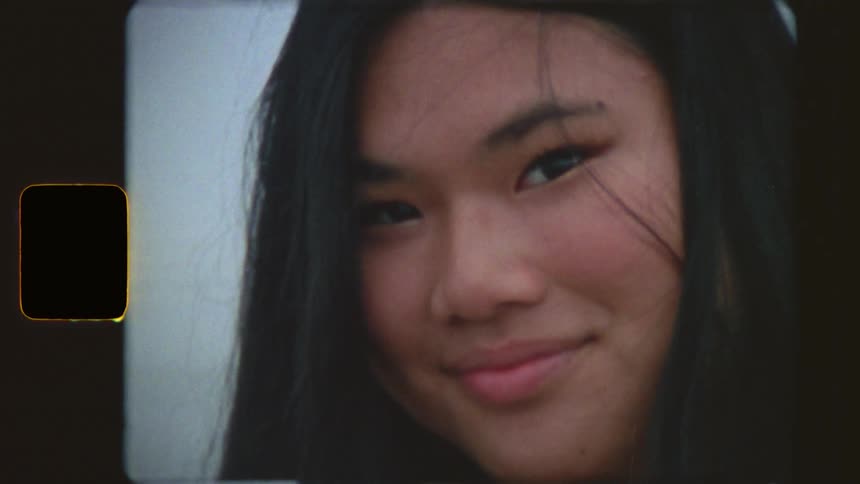 A vintage-style, super 8 film portrait of a beautiful young woman smiling gently while standing in the ocean on an overcast day
