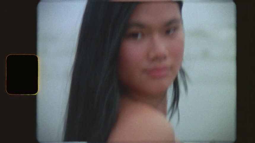 An authentic Super 8 film portrait of a beautiful young woman with long black hair looking at the camera by the water