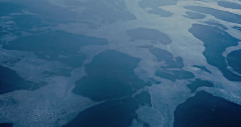 A serene, high-angle view of white sea foam drifting on calm, deep blue ocean water