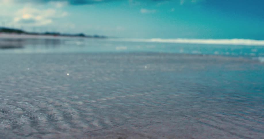 A low-angle, shallow-focus view of calm ocean water rippling over wet sand on a serene beach