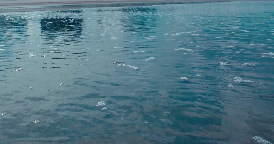 A serene close-up of tranquil blue water gently rippling at the edge of a sandy shoreline