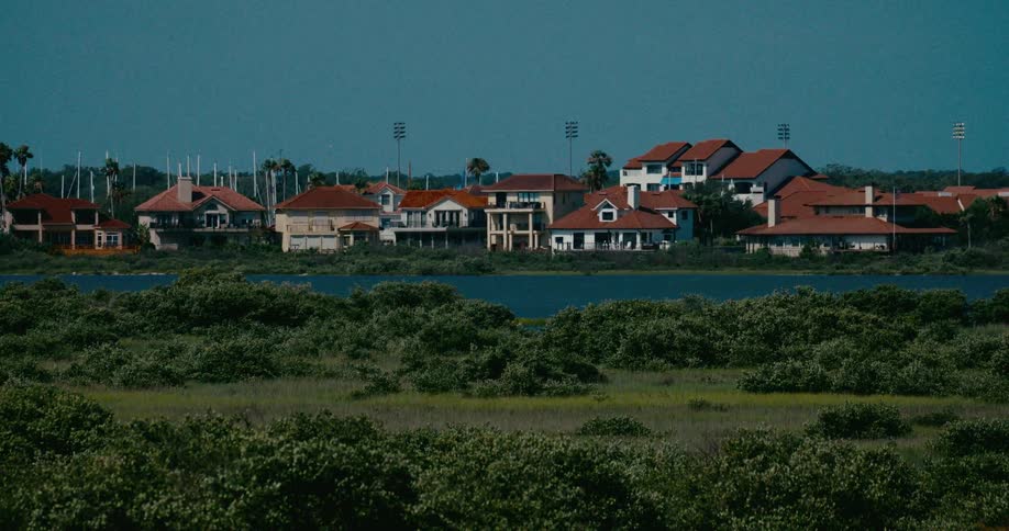 A serene view of an affluent coastal neighborhood across a bay, with a lush green marshland in the foreground