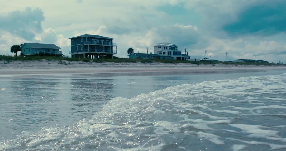 Tranquil ocean waves wash onto the shore in super slow motion with beachfront houses reflected in the water