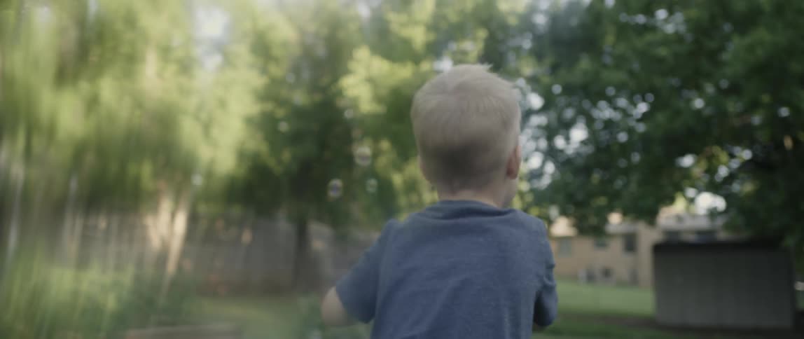 Toddler runs in a yard blowing bubbles