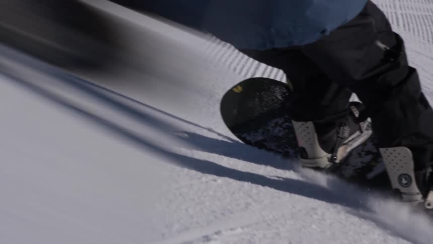 Close-up slow motion shot of a snowboarder carving down a snowy slope on a sunny day