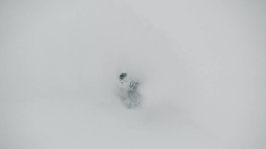 High-angle slow motion shot of a snowboarder riding through deep powder snow and getting completely enveloped in a white cloud