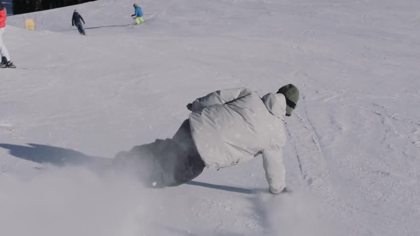 A snowboarder leans into a sharp carve down a snowy slope, kicking up a spray of powder in slow motion