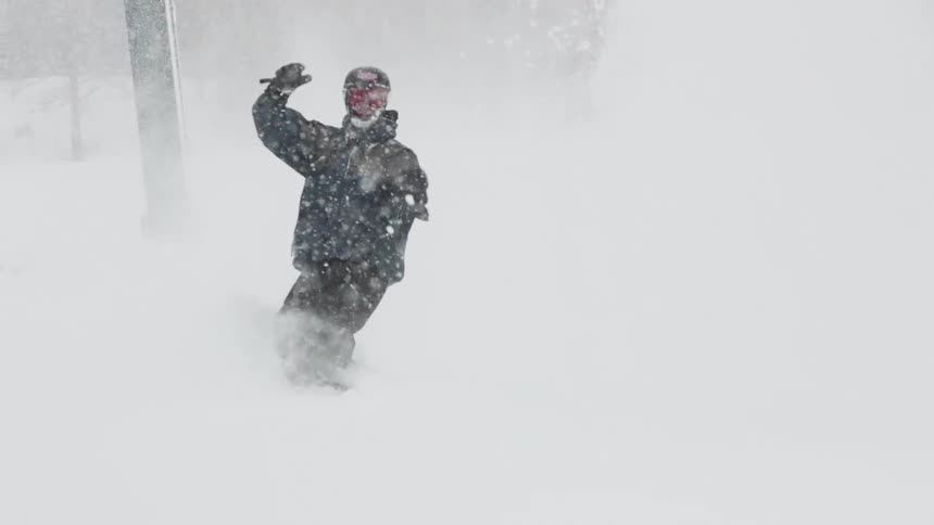 A snowboarder carves a deep turn in fresh powder, sending a huge cloud of snow toward the camera in super slow motion