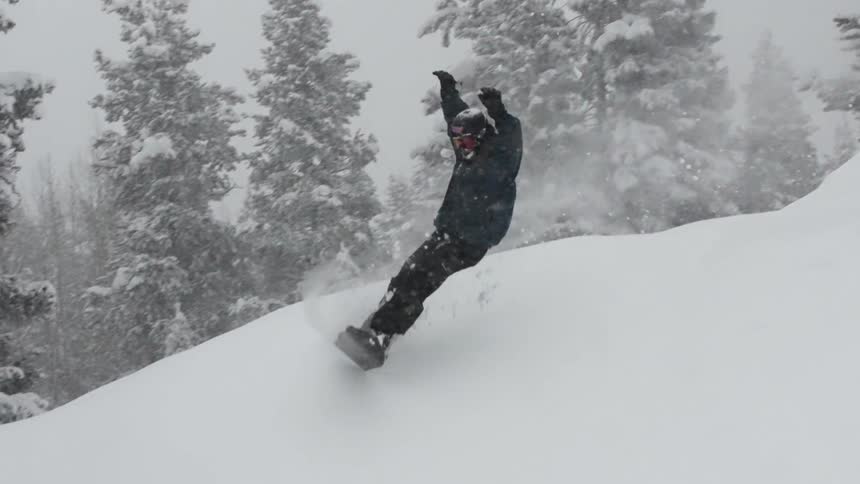 A snowboarder launches off a snow-covered feature and carves through deep powder during a snowstorm in super slow motion