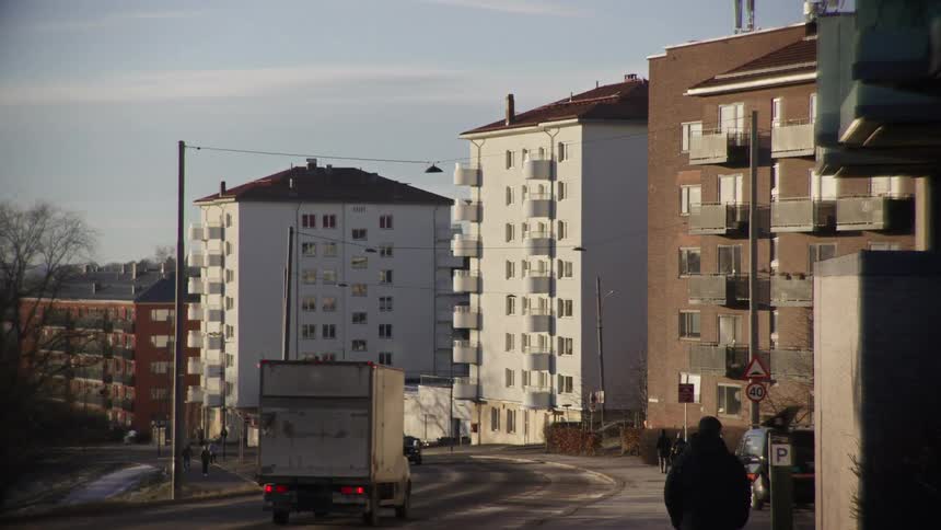 A person walks down a quiet city street lined with apartment buildings as a truck drives by on a clear day