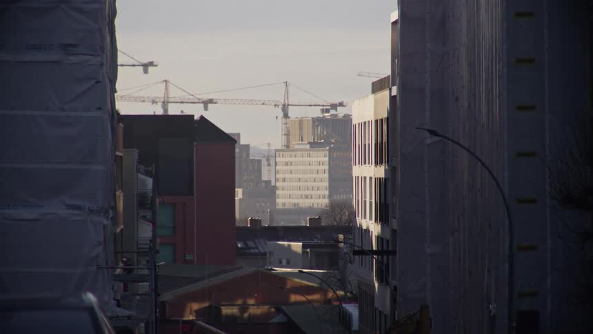A slow zoom down a city street reveals construction cranes towering over the urban landscape