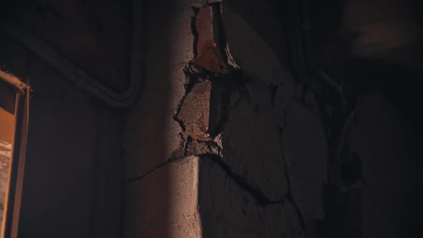 A slow push-in reveals a large crack in the decaying wall of a dark and mysterious attic lit by a single lightbulb