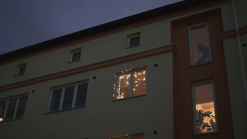 Colorful disco ball lights illuminate a single apartment window on an otherwise quiet building at night