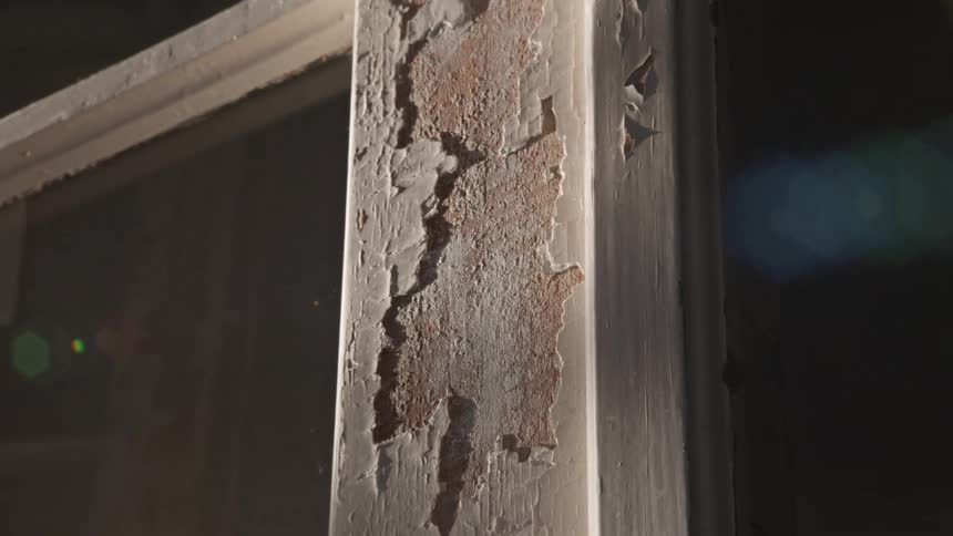 A slow zoom reveals the decaying, peeling paint on a sunlit vintage window frame as dust motes float by