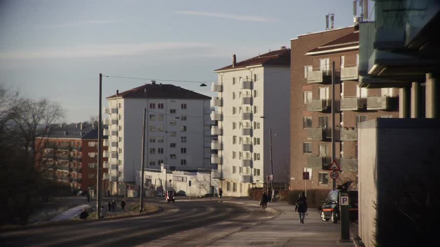 A quiet residential street with apartment buildings where people walk and cycle on a sunny day