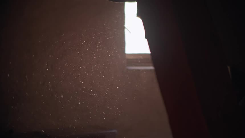 Golden dust particles slowly dance and float through a warm beam of sunlight in a dark room