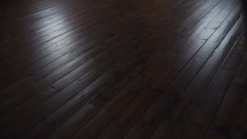 A slow zoom out on a dark, glossy hardwood floor with soft light reflections