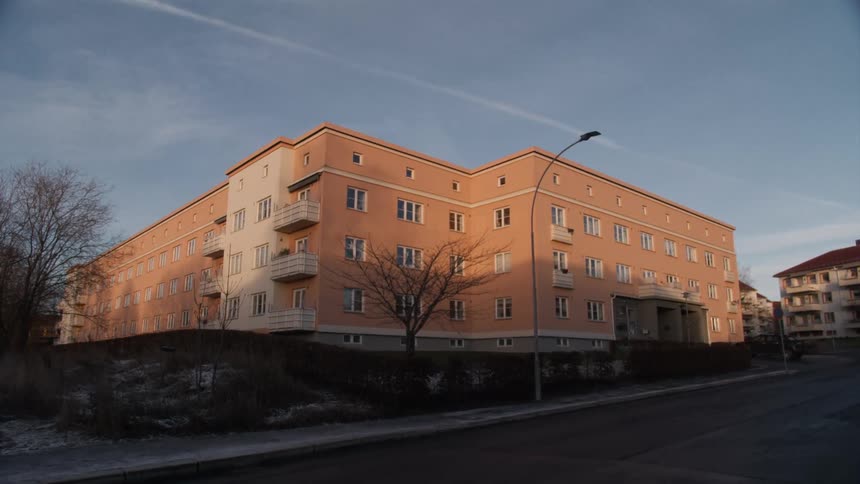 A warm, pinkish-orange apartment building sits peacefully on a quiet street corner on a cold, sunny day