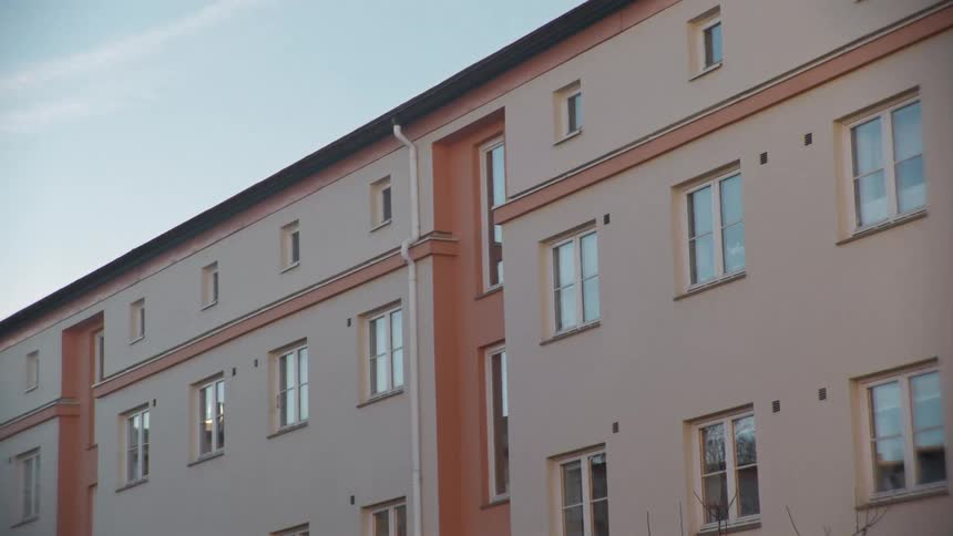 A slow zoom-in on the clean facade of a modern apartment building with peach accents against a clear sky