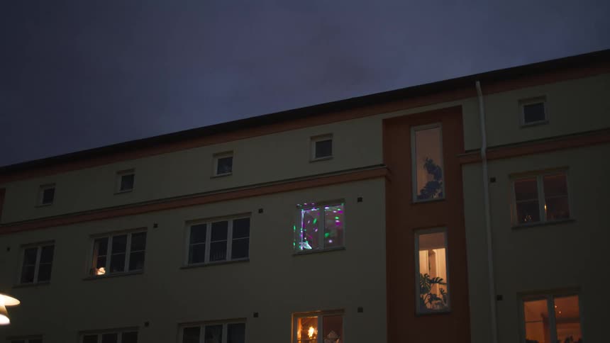Colorful disco lights from a lone party stand out in an apartment building window at night