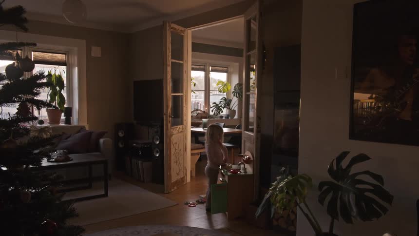 A little girl plays in a sun-drenched living room with a Christmas tree during the holidays