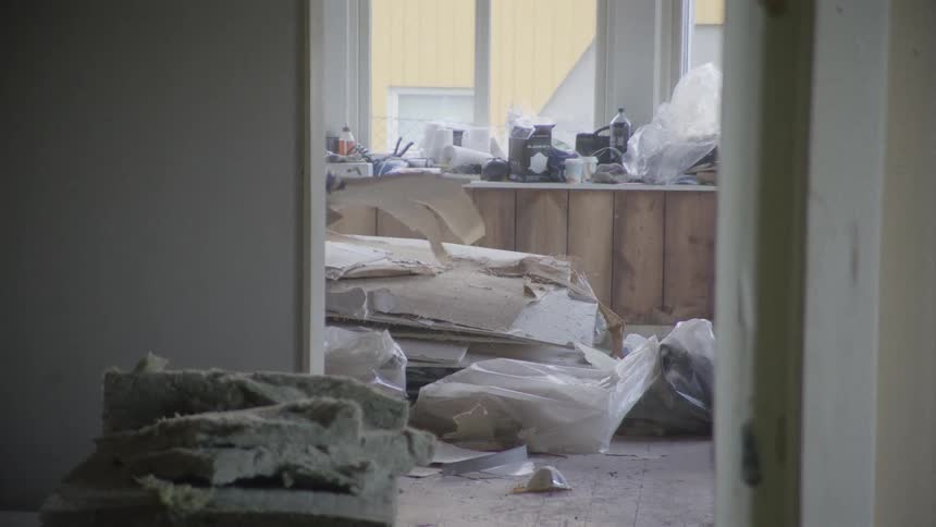 View through a doorway of a messy room under renovation, with insulation and construction debris cluttering the floor