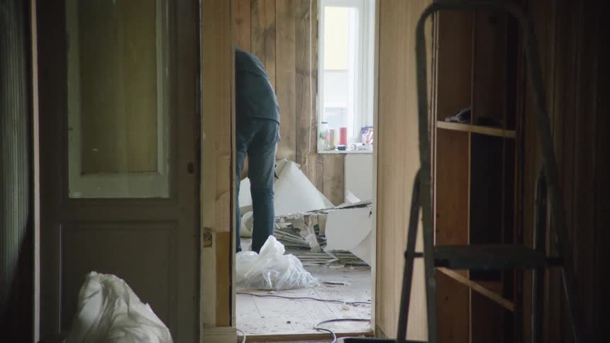 Slow dolly shot from a dark hallway shows two men cleaning up debris inside a house during a major renovation