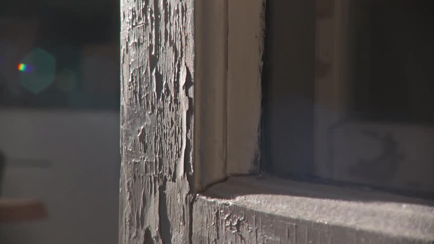 A slow camera move reveals the detailed texture of peeling paint on an old, sunlit wooden door frame