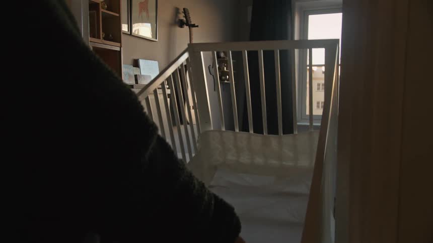 A man in slow motion carefully carries a white baby crib into a sunlit bedroom, preparing a nursery for a new arrival