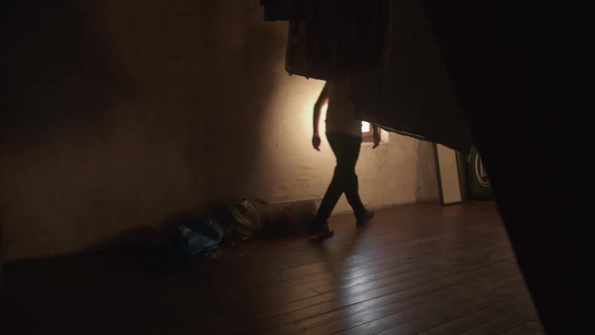 A person empties a box of dust and debris onto a wooden floor, with particles floating through a sunbeam in slow motion