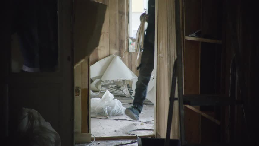 A construction worker tears down walls and carries debris out of a messy room during a home renovation in slow motion