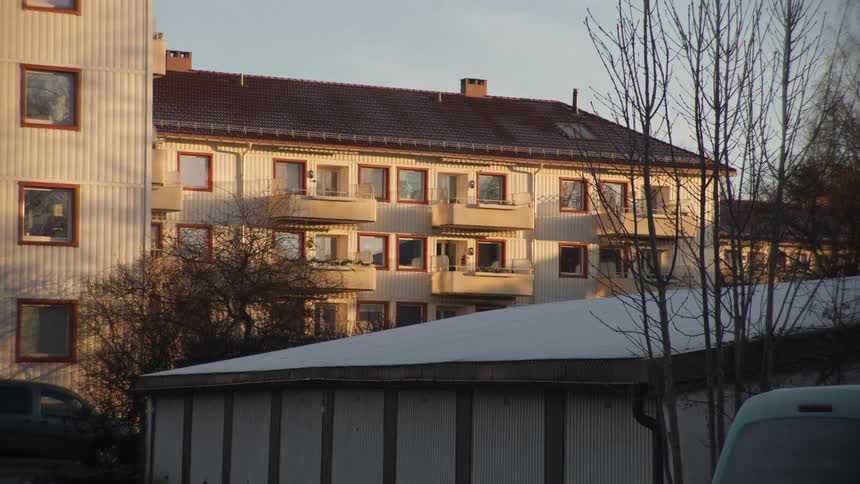 A slow zoom timelapse captures the setting sun casting long shadows across a quiet residential apartment complex in winter