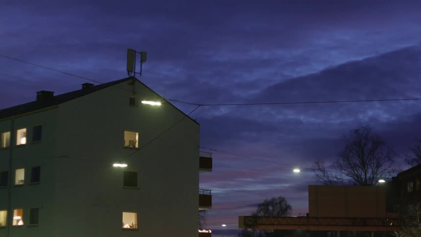 A white apartment building is illuminated by streetlights under a deep blue twilight sky