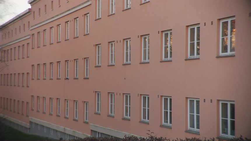 A slow zoom out on the uniform exterior of a large, pink, institutional-style building with many windows