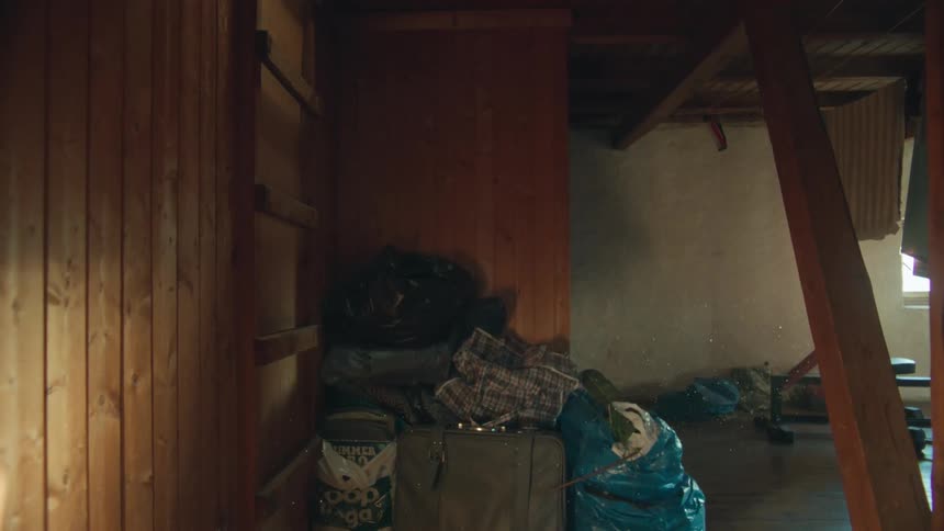 Slow tilt down revealing a dusty, messy corner in a wooden attic with floating dust particles