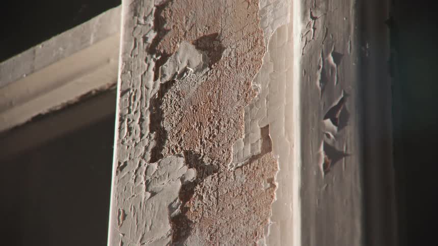 A close-up view of shifting shadows on an old wooden frame with cracked and peeling paint