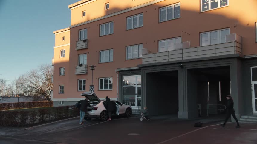 Slow zoom-in on a family unpacking their car outside a modern apartment building on a sunny day