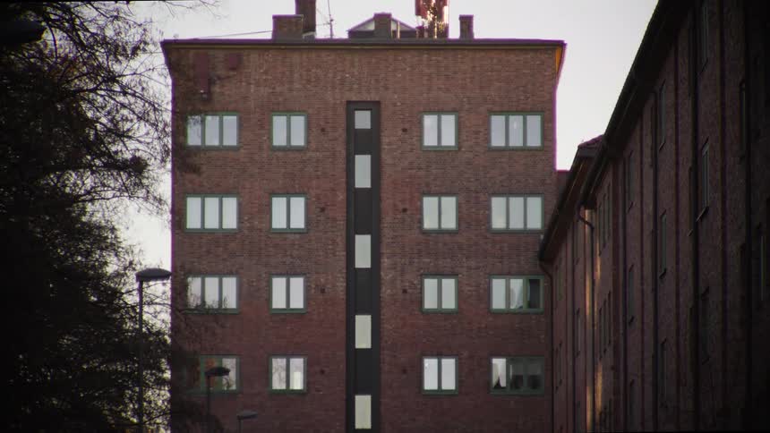 A slow tilt-up reveals the full facade of a classic red brick apartment building with green-trimmed windows