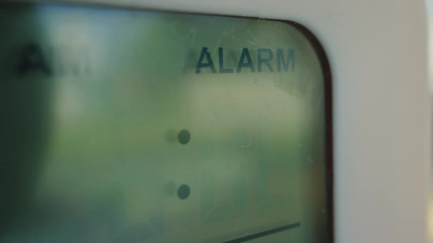 A close-up of a digital alarm clock flashing 6:00 AM as the alarm goes off
