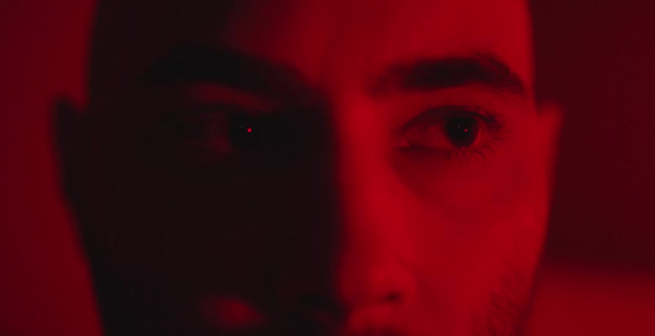 Extreme close-up on a man's intense gaze under dramatic, shadowy red light