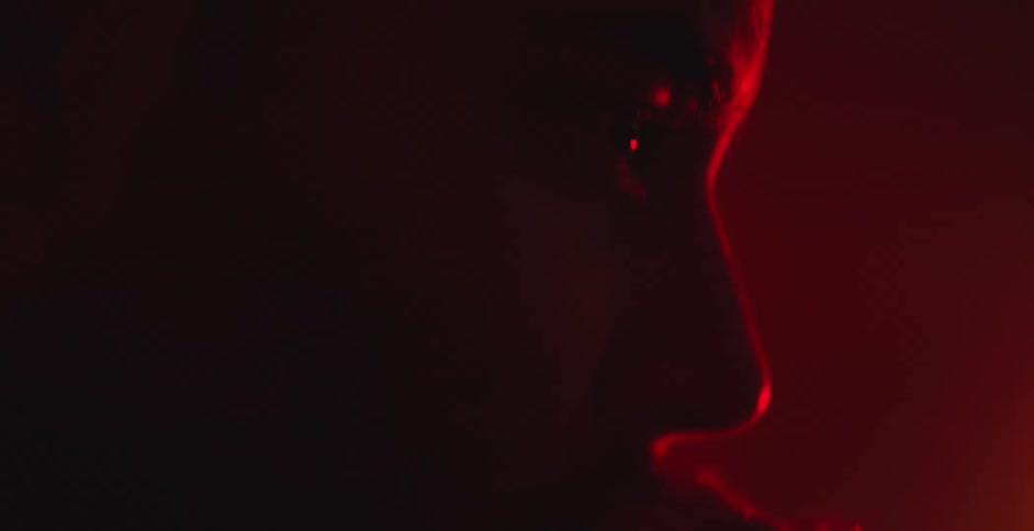 Mysterious close-up shot pans down a man's face, silhouetted against a dramatic red light