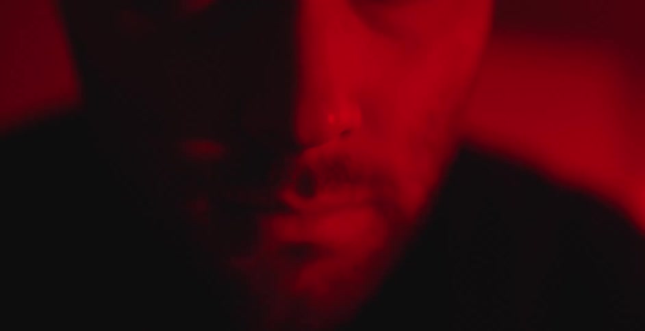 A mysterious man's shadowed face is lit with a dramatic and moody red light