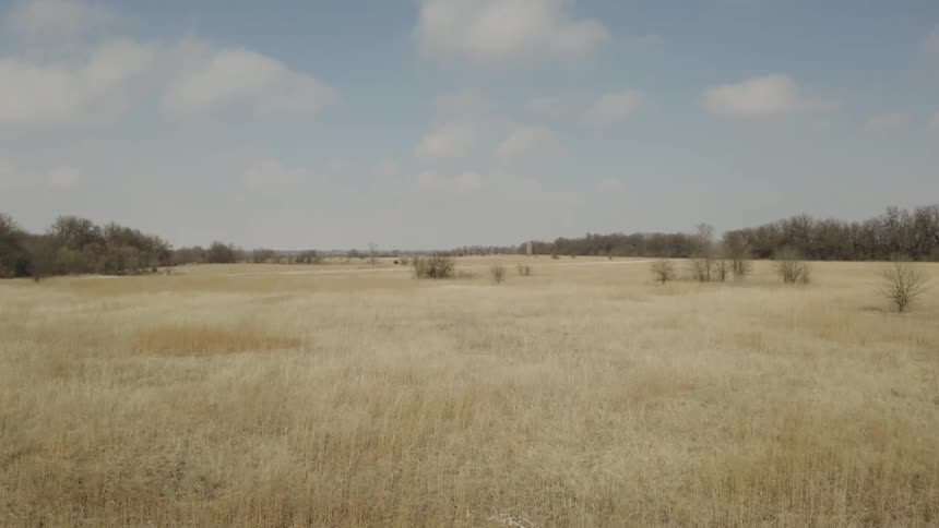 Low aerial dolly shot over a vast, golden prairie with patches of snow on a clear winter day