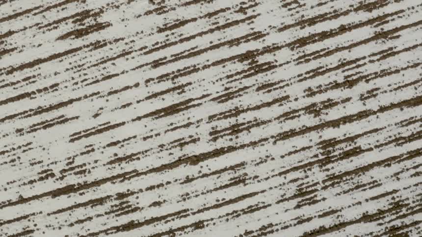 An aerial top-down perspective reveals the abstract linear patterns of a snow-covered agricultural field
